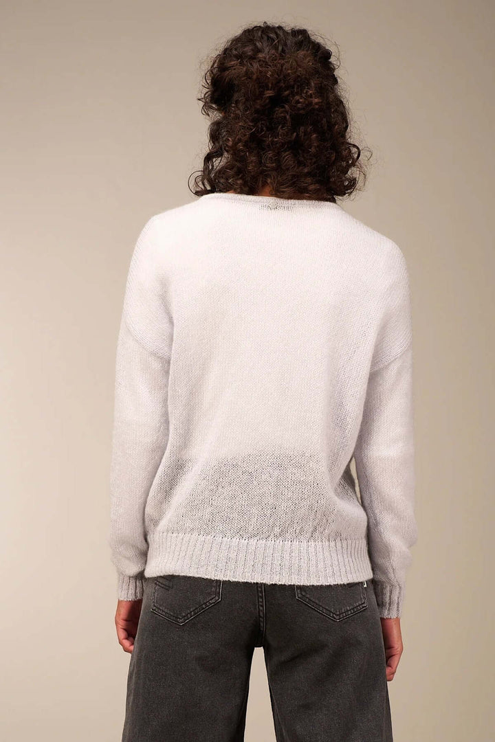 Person wearing a light, airy knit sweater in white with decorative buttons, paired with high-waisted denim, showcasing a casual fall style.