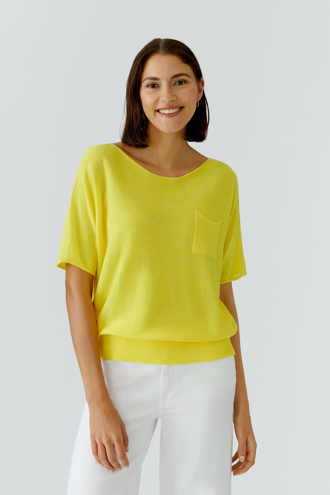 Femme portant tricot fluide à manches courtes jaune avec poche poitrine et encolure dégagée, style décontracté et moderne.