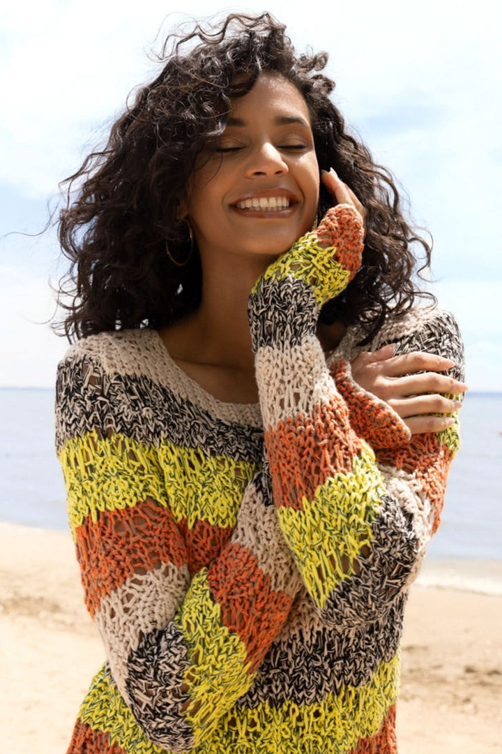 Femme souriante portant un tricot rayé texturé au style artisanal sur la plage, idéal pour la mi-saison, en coton léger et respirant.