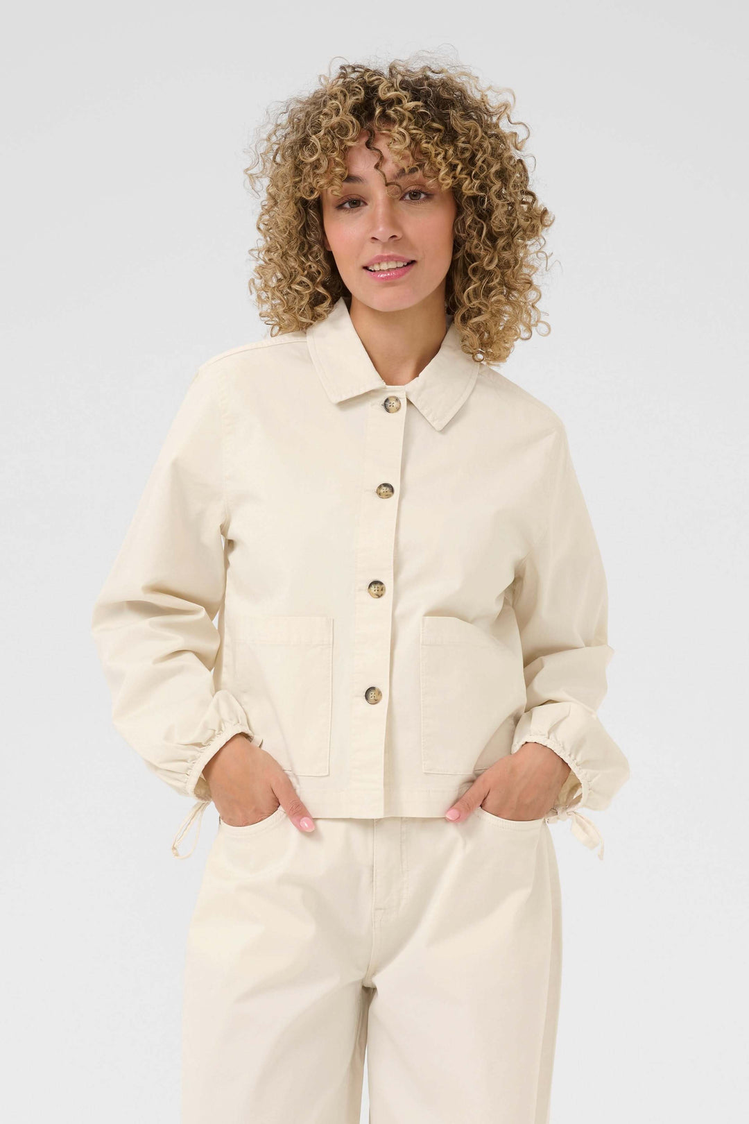 Veste Berta beige légère avec col chemise, boutons et poches, portée sur t-shirt pour un look décontracté.