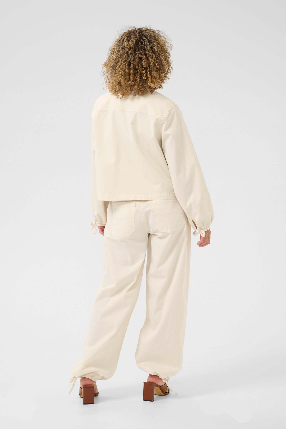 Veste Berta beige, coupe droite, manches froncées, portée avec pantalon assorti, vue arrière.