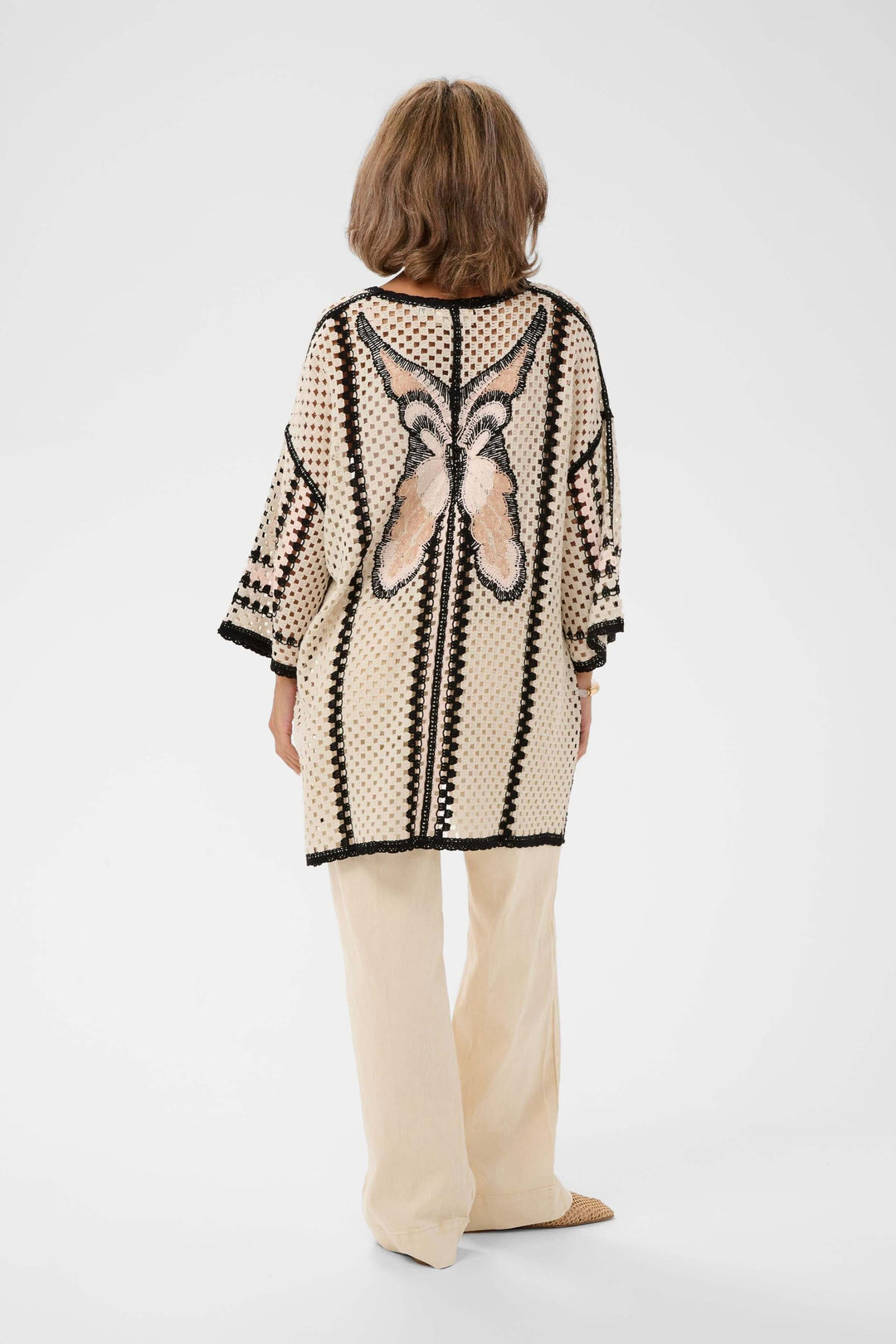 Femme portant une Veste Free ouverte en crochet avec motif ajouré, manches larges trois-quarts, et bordures contrastantes.