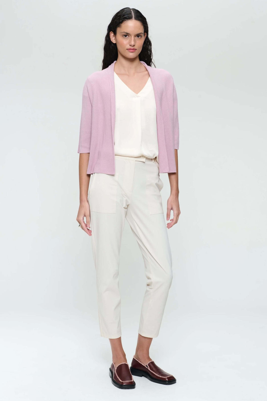 Femme portant une veste sans manches rose avec un haut blanc et un pantalon clair, style décontracté-chic.