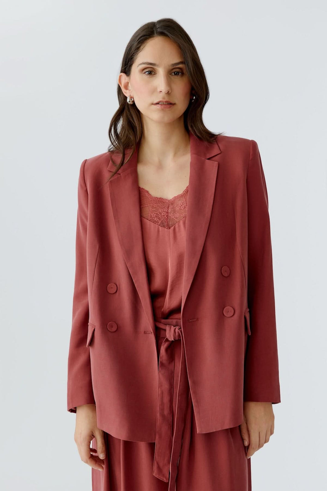 Femme portant une veste blazer structurée croisée rouge avec double boutonnage et coupe droite, idéale pour un look élégant et moderne.