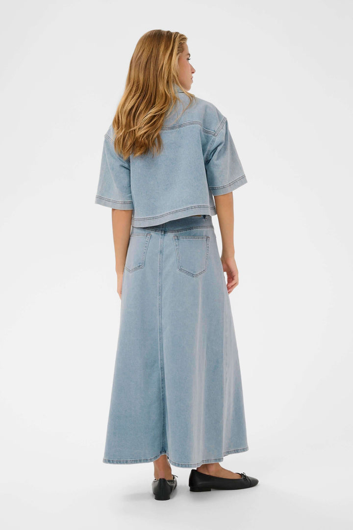 Femme portant une veste courte en denim à manches courtes, vue de dos, avec une jupe longue assortie, style décontracté et moderne.
