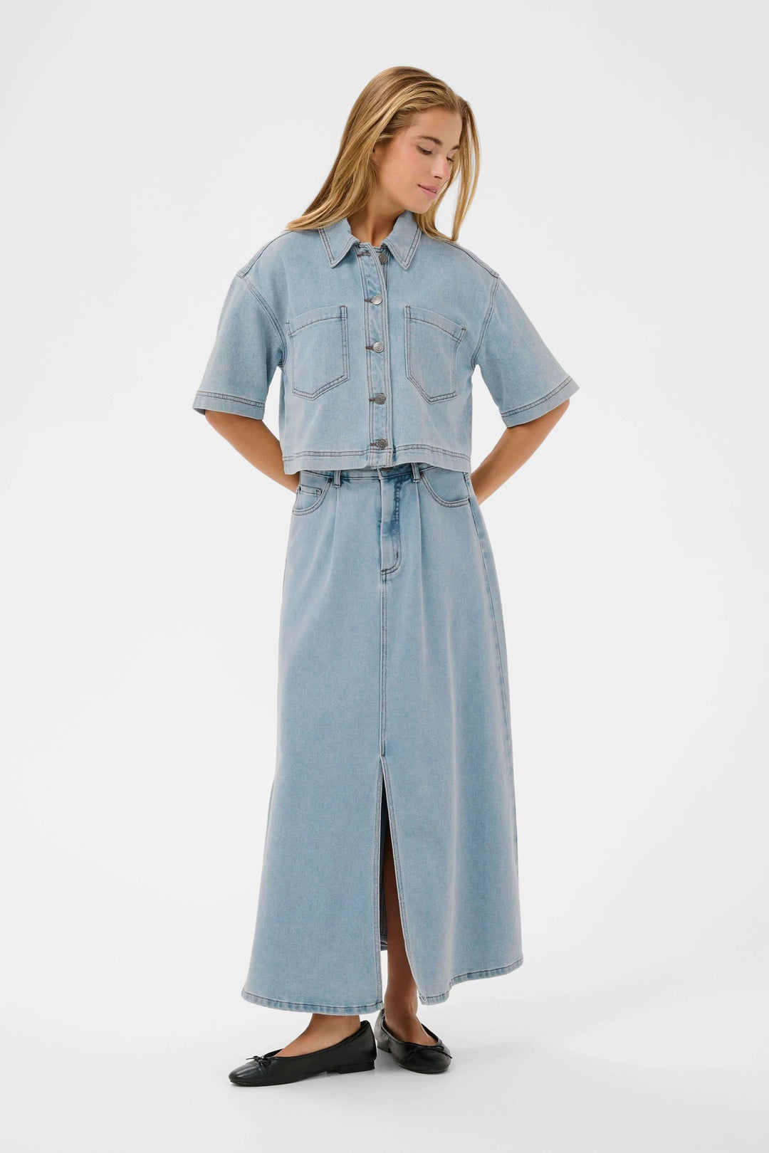 Veste courte en denim à manches courtes portée par une femme avec une jupe longue. Tissu robuste et coupe moderne pour un style décontracté.