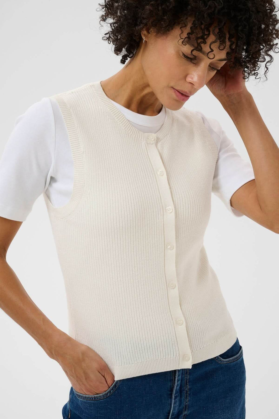 Femme portant la Veste de tricot Gemma, haut sans manches en maille fine avec patte de boutonnage et encolure ronde, allure minimaliste.