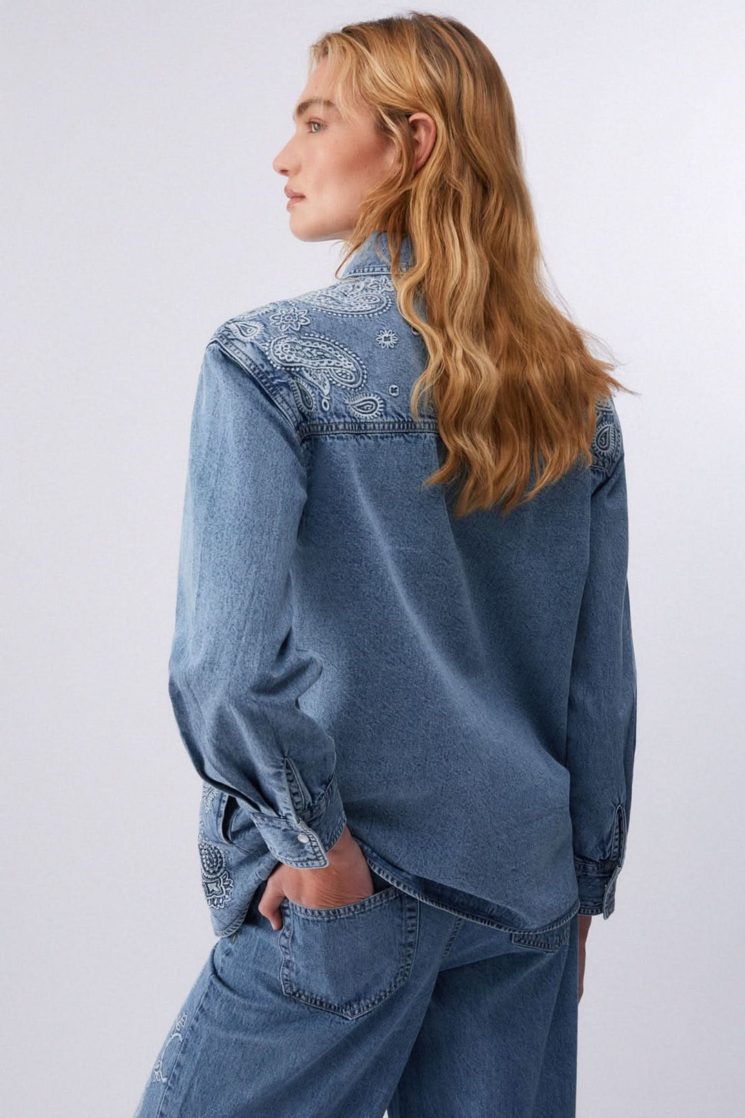 Veste en jean imprimée à boutons pression avec motif audacieux au dos, portée par une femme de dos, style moderne et confortable.