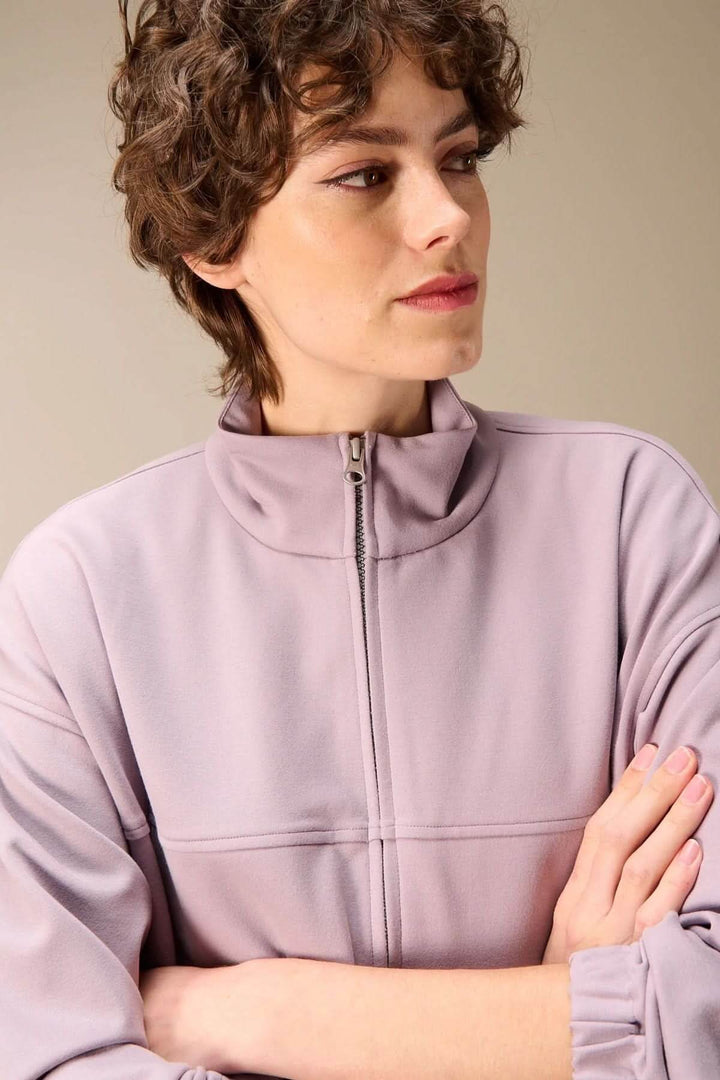 Femme portant une veste en sweat avec fermeture éclair, col montant structuré, couleur lavande.
