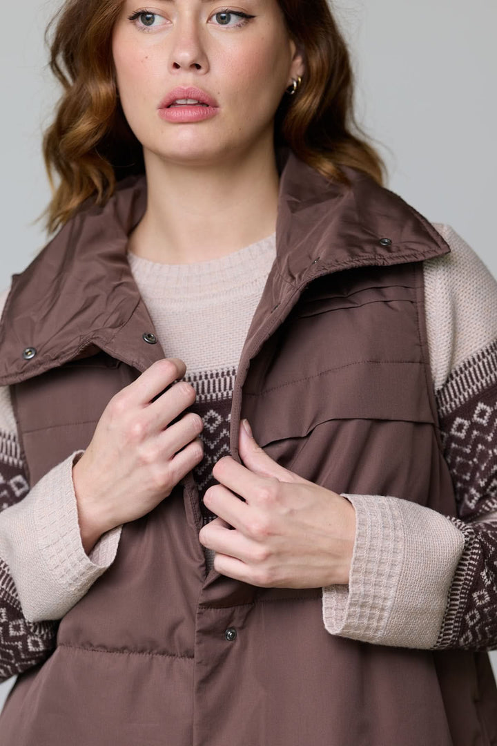 Femme portant une veste sans manches matelassée marron avec un col montant et un pull à motifs pour la mi-saison.