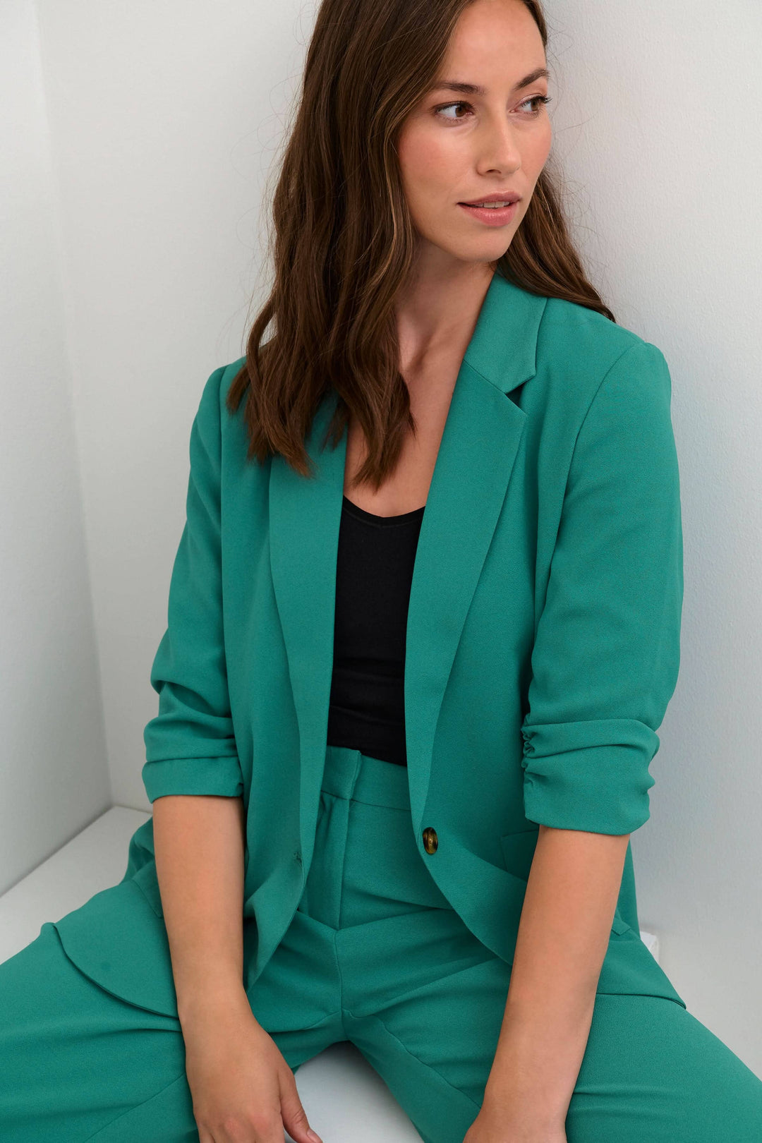 Femme portant un veston cocamia turquoise avec un top noir, style décontracté et professionnel.