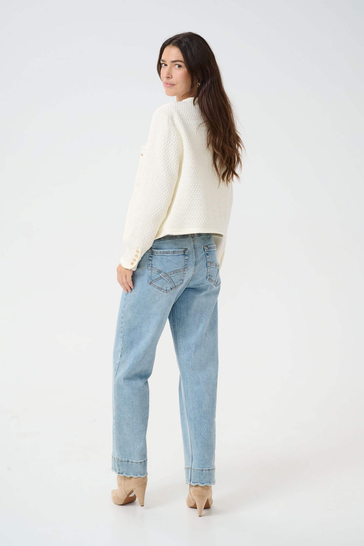 Femme portant un veston structuré écru, jean décontracté et talons, vue de dos.