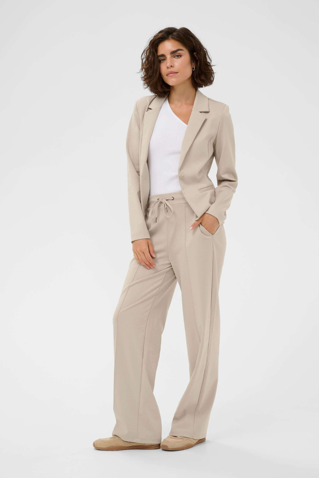 Veston Jenny structuré porté par une femme, offrant une silhouette élégante et féminine, avec pantalon beige pour un look décontracté.