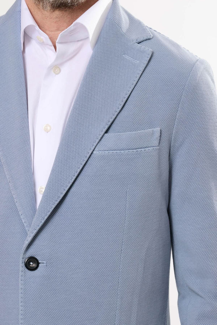 Veston en maille texturée bleu avec fermeture à deux boutons et poches avant, porté sur une chemise blanche.