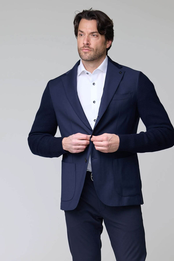 Homme portant un veston hybride tricot et tissu élégant avec manches en maille et col à revers, style moderne et sophistiqué.