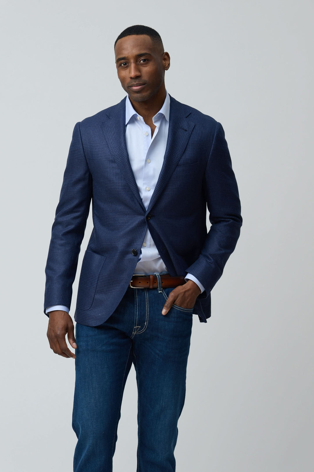 Homme portant un veston structuré à motif subtil avec chemise blanche et jean pour un style moderne et élégant.