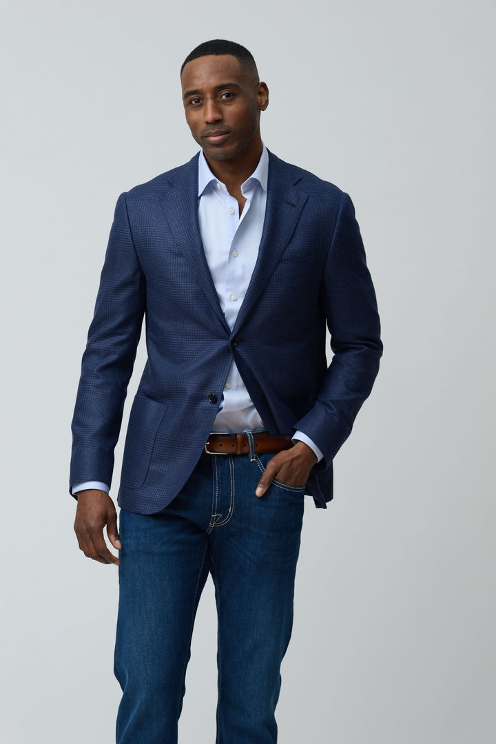 Homme portant un veston structuré à motif subtil avec chemise blanche et jean pour un style moderne et élégant.