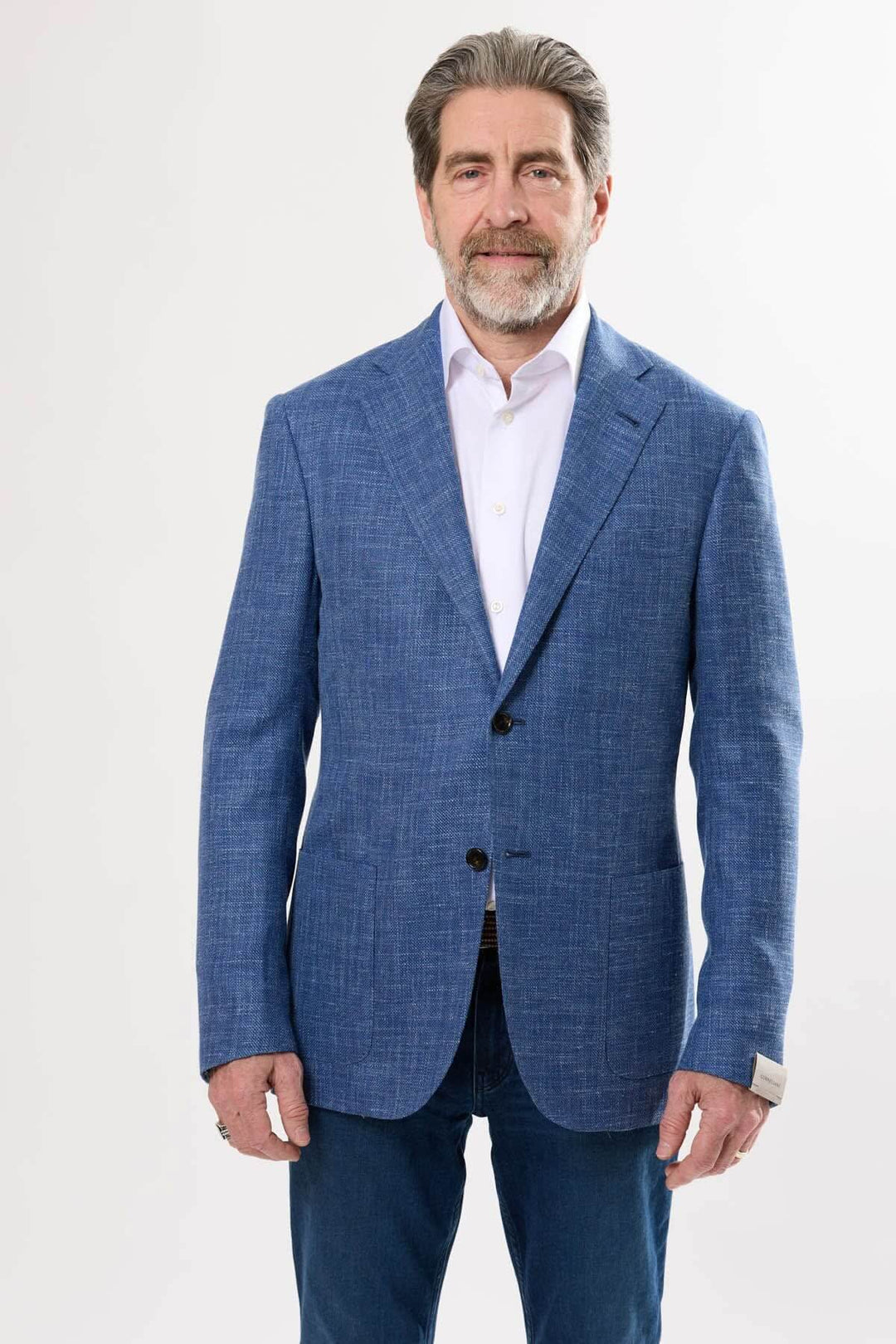 Homme portant un veston texturé bleu avec poche, chemise blanche et jeans, équilibre de sophistication et décontraction.