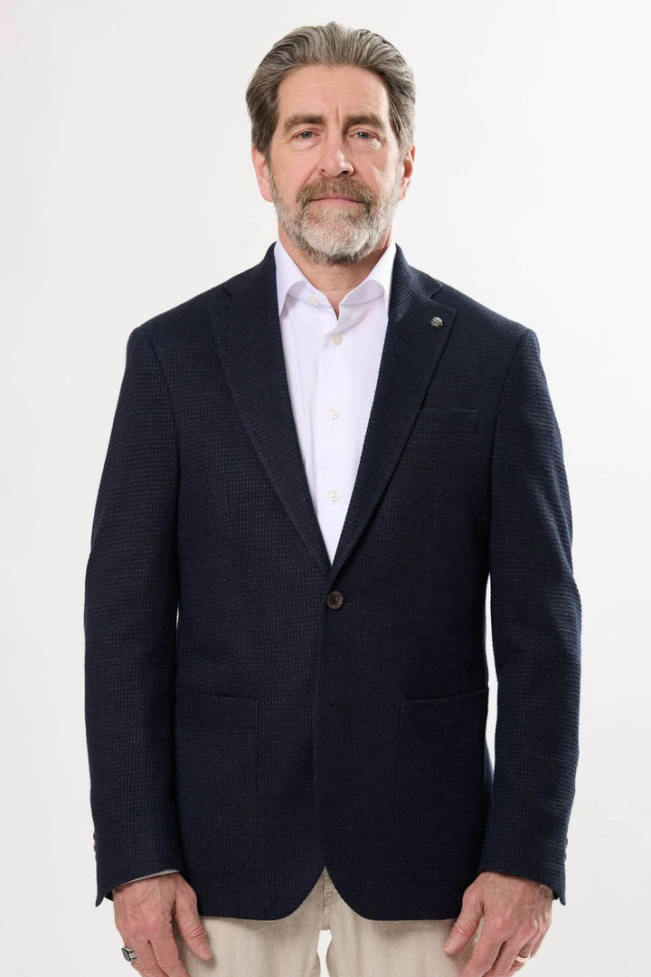 Homme portant un veston texturé bleu avec col à revers cranté et boutons, parfait pour les événements élégants.