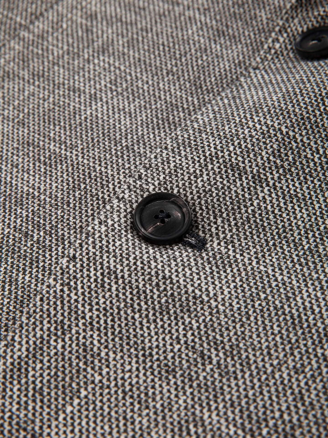 Gros plan sur le tissu et le bouton en corne du veston texturé, mettant en valeur sa texture raffinée.