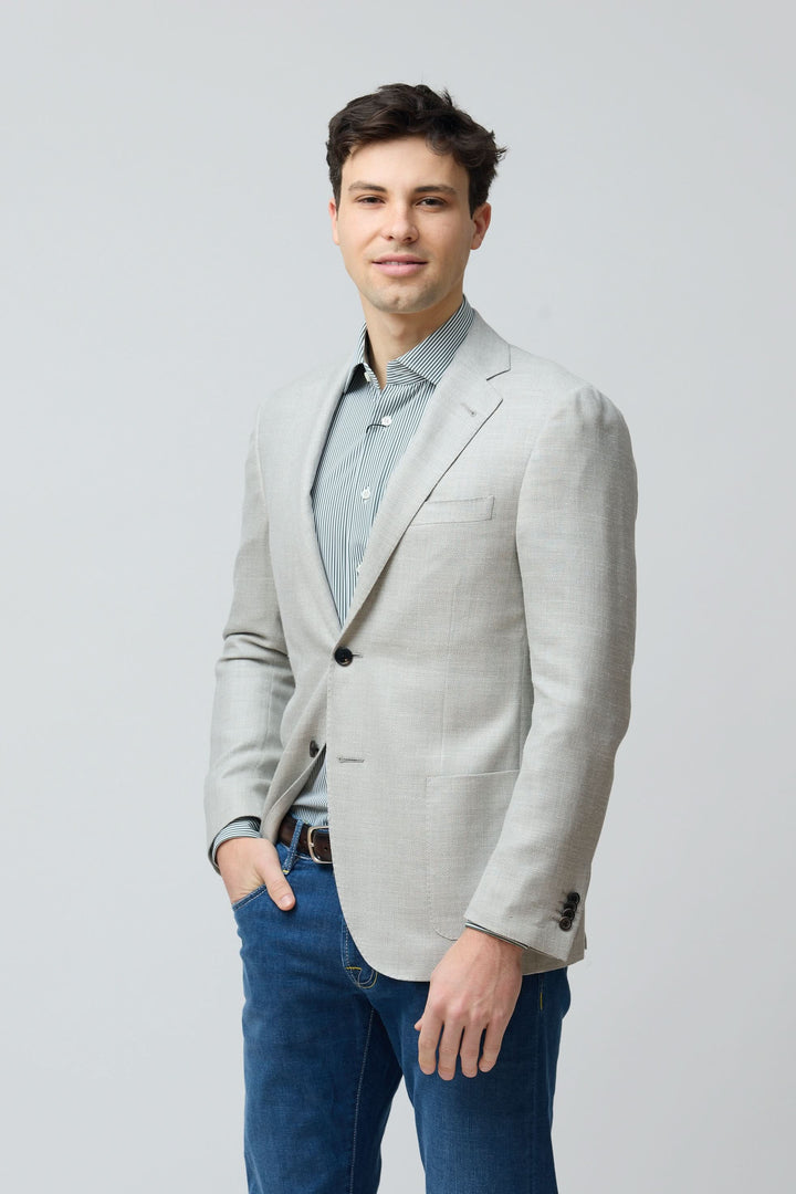 Homme portant un veston texturé en laine, soie et lin avec chemise bleue et jeans, style décontracté élégance.