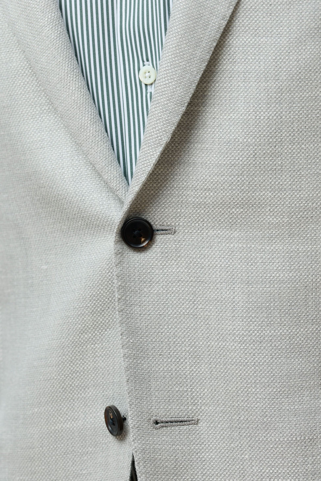 Détail du veston texturé en laine, soie et lin avec boutonnière et motifs à rayures en dessous.