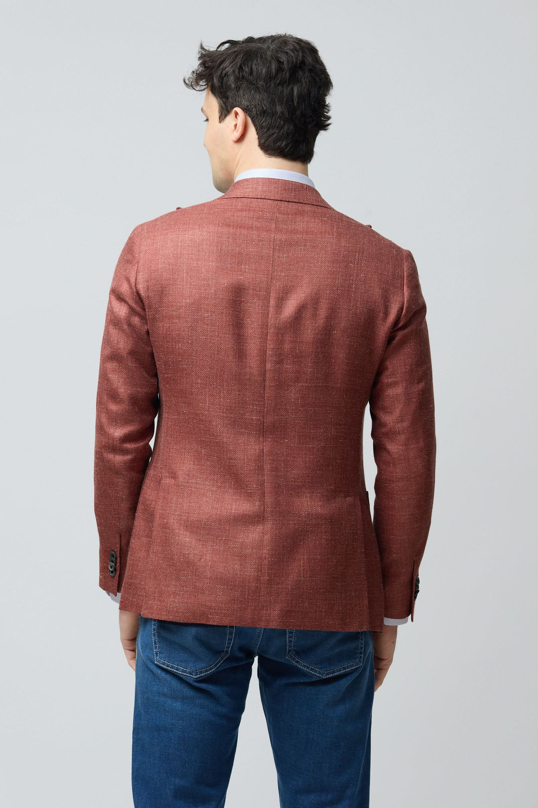 Homme portant un veston texturé en laine, soie et lin de couleur rouille, coupe ajustée, vue de dos, style décontracté chic.