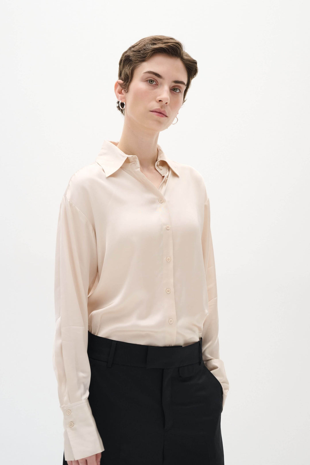 Chemise satinée Pauline, ample et chic, portée avec un pantalon noir pour un style décontracté et élégant.