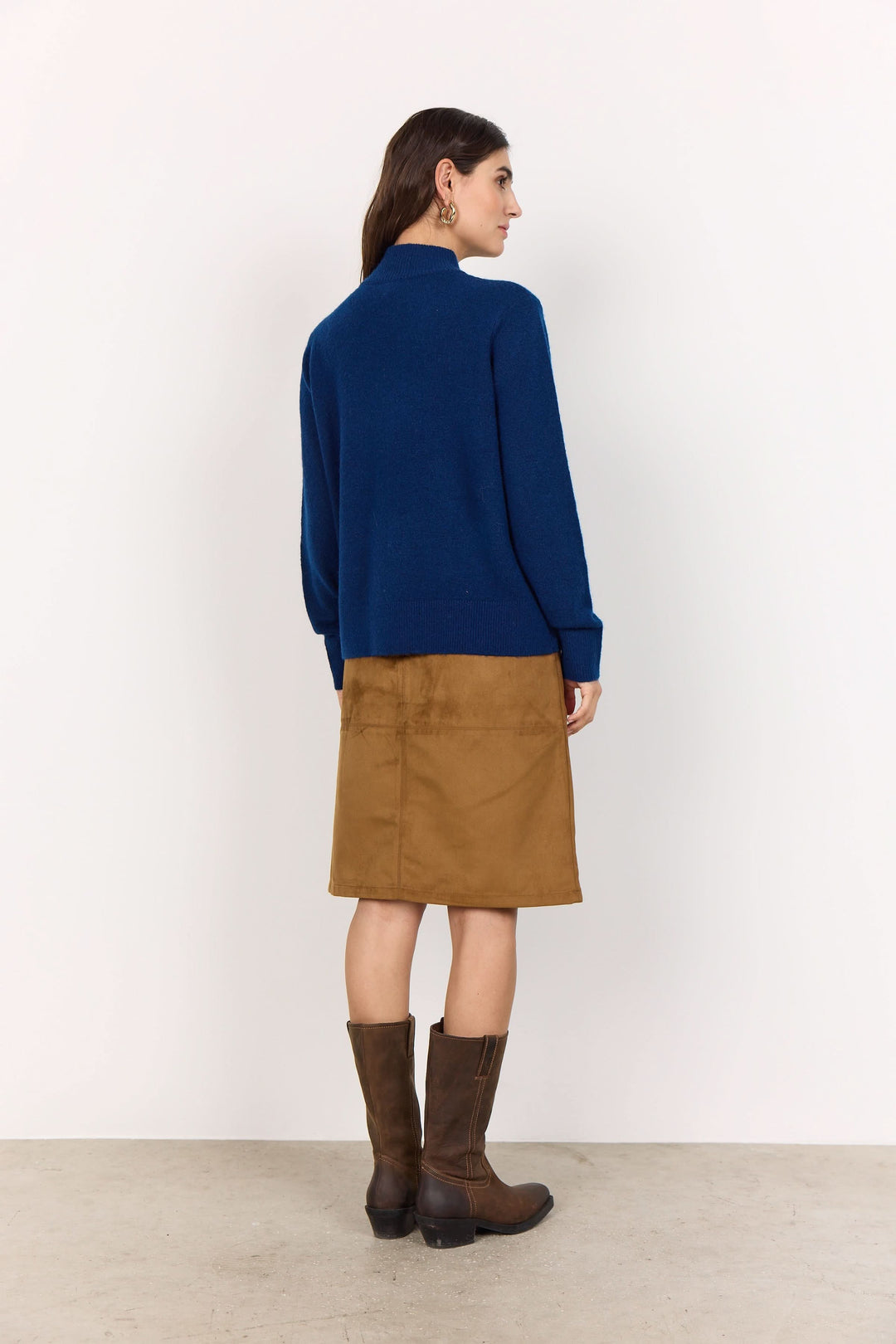 Femme portant un cardigan zippé bleu avec une jupe en suédine et des bottes marron, vue arrière.