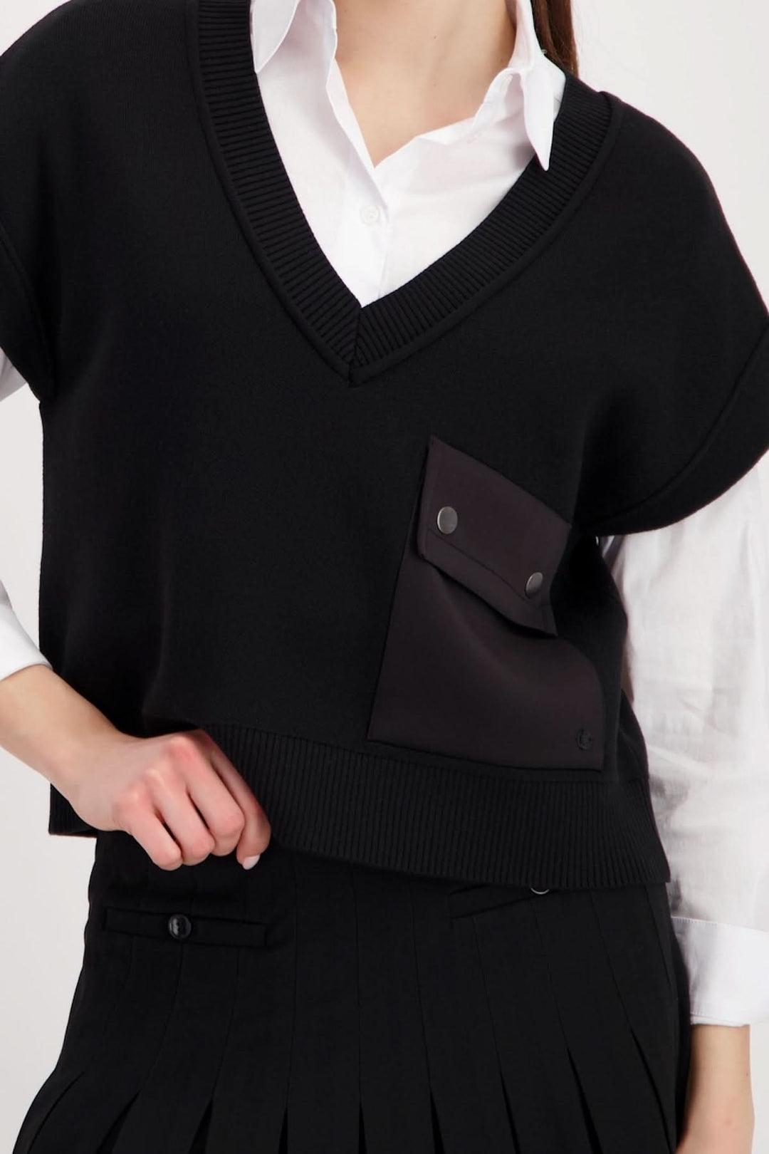 Femme portant un haut sans manches au col en V avec poche avant, superposé à une chemise blanche, style chic et moderne.