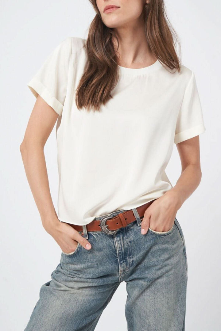 Femme portant une blouse en soie blanche avec manches courtes à revers et encolure ronde, style chic et décontracté.