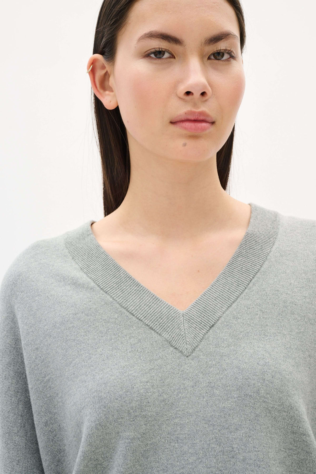 Femme portant un chandail col en V gris en coton, à coupe décontractée et finitions soignées.