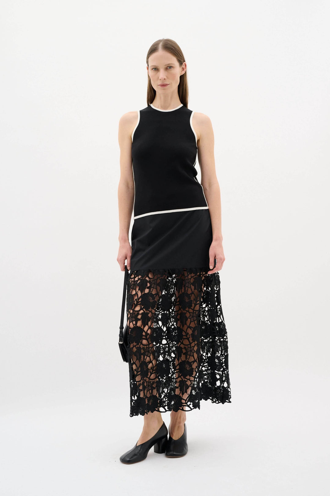Modèle portant un camisole noir à encolure ronde, associé à une jupe en dentelle noire, look minimaliste et raffiné.