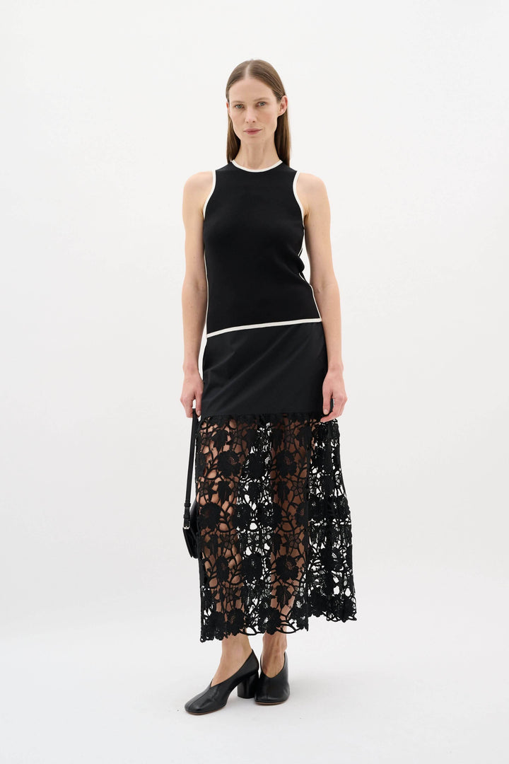 Modèle portant un camisole noir à encolure ronde, associé à une jupe en dentelle noire, look minimaliste et raffiné.