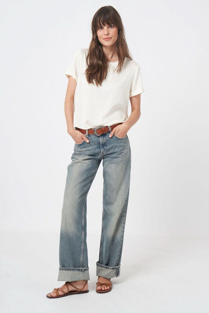 Person wearing casual outfit with a white blouse and light denim jeans, standing against a plain background.