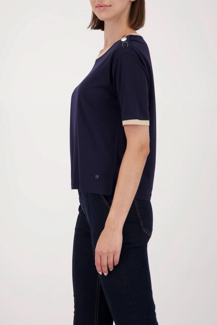 Femme portant un t-shirt à boutons décoratifs sur l’épaule en jersey doux avec finition contrastante, idéal pour un style chic ou décontracté.