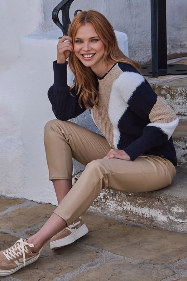 Femme portant un chandail en maille à motif graphique, col rond, avec un pantalon beige, assise extérieur sur des marches en pierre.