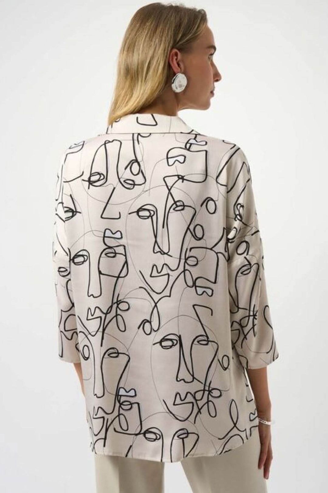 Blouse imprimée graphique avec motifs abstraits de visages, col chemise ouvert et manches mi-longues.