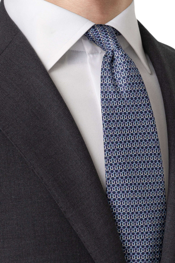 Cravate à motif géométrique bleue portée avec un complet gris anthracite et une chemise blanche.