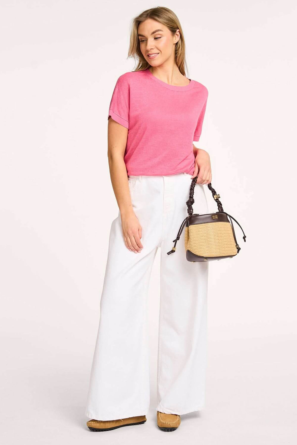 T-shirt léger à col rond rose, porté avec un pantalon blanc ample et un sac à main, look décontracté et estival.