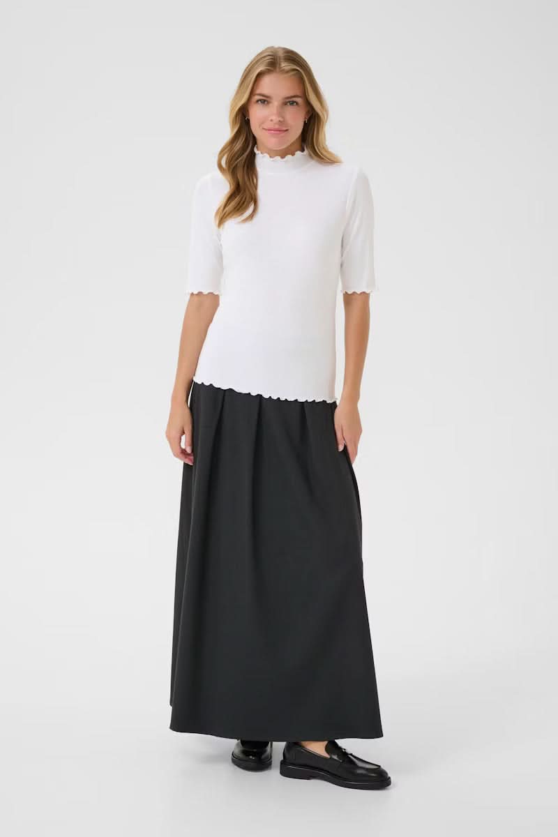 Femme portant un T-shirt Ribba blanc à col montant festonné, maille côtelée, manches mi-longues, avec jupe longue noire et mocassins.