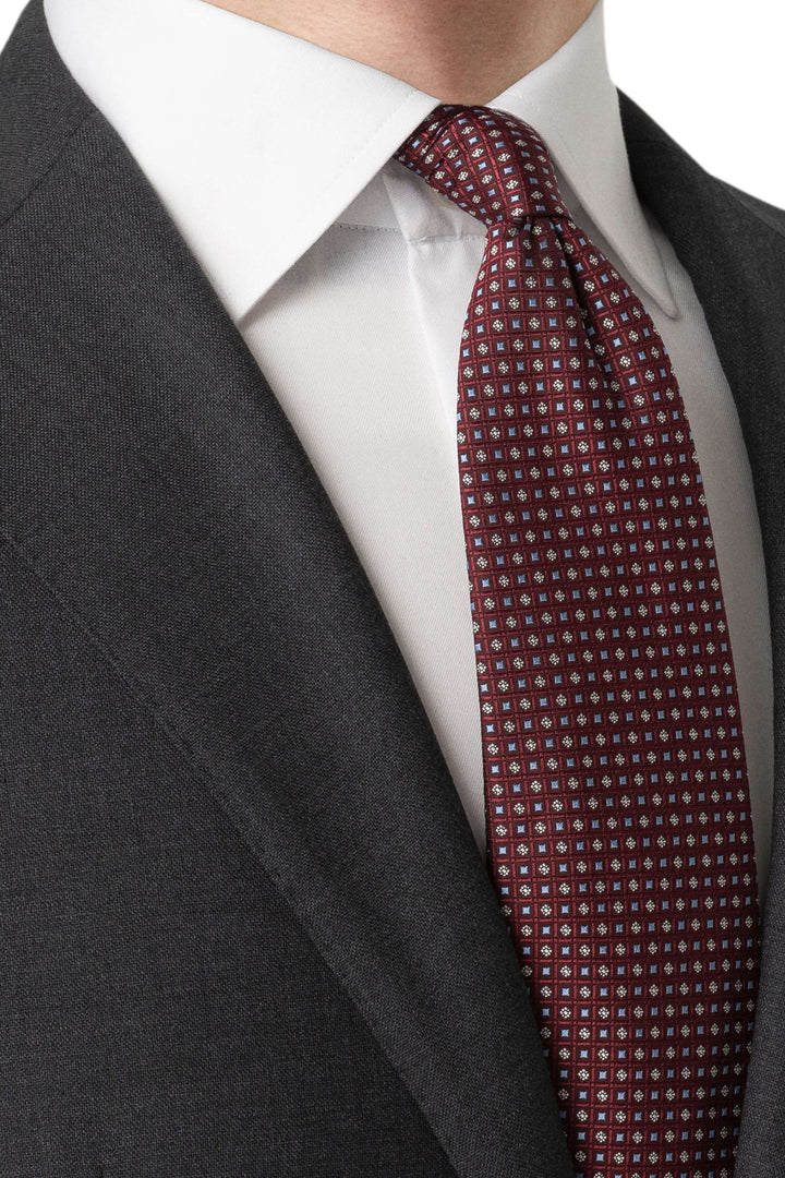 Cravate à motif géométrique portée avec un costume gris et une chemise blanche. Élégance intemporelle.