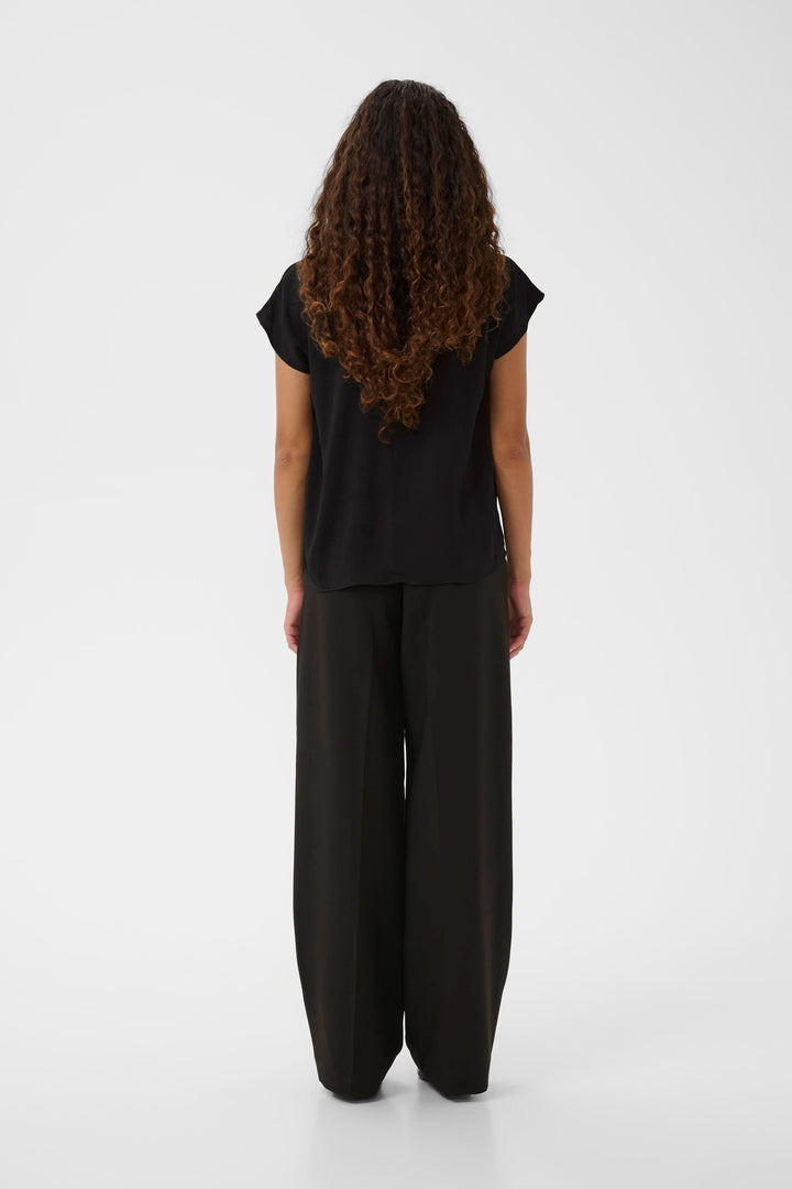 Vue arrière d'une femme portant un haut noir décontracté avec un pantalon ample, coiffée de cheveux bouclés.