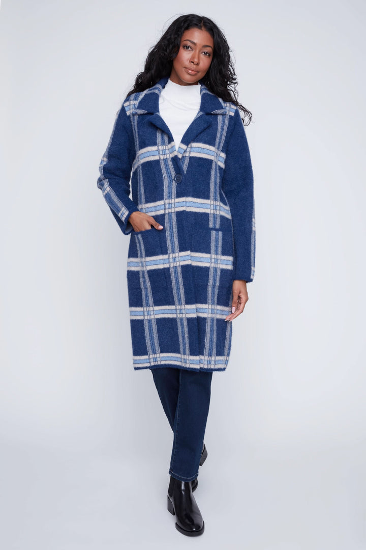 Manteau long à carreaux bleu avec col à revers, porté sur un col roulé et pantalon ajusté, style chic et moderne.