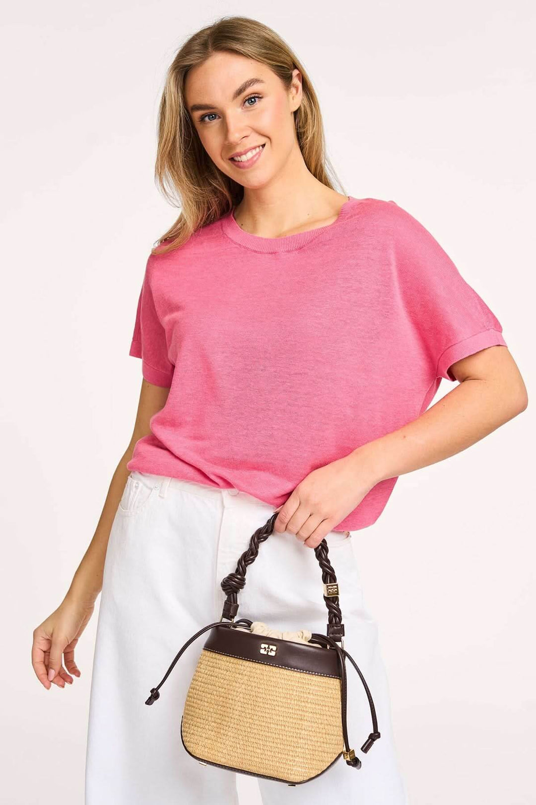 Femme souriante portant un t-shirt rose et un sac à main en osier, look décontracté et moderne.