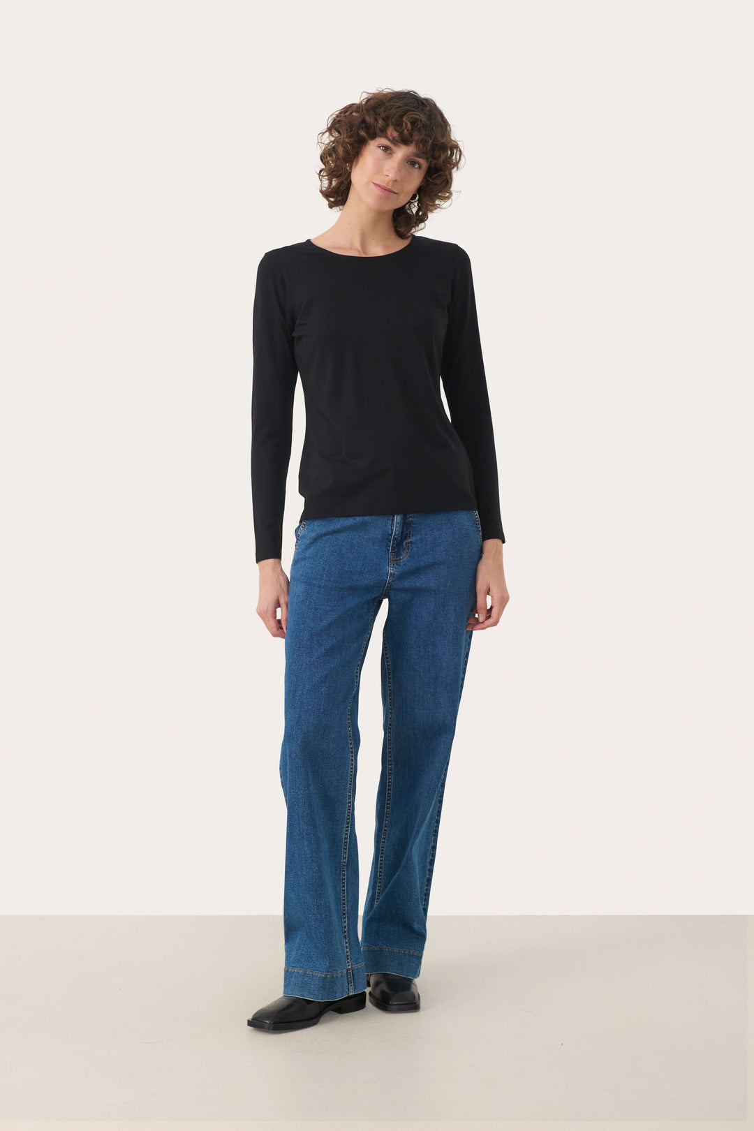 Femme portant un chandail noir à manches longues et un jean bleu, montrant un style décontracté et élégant.