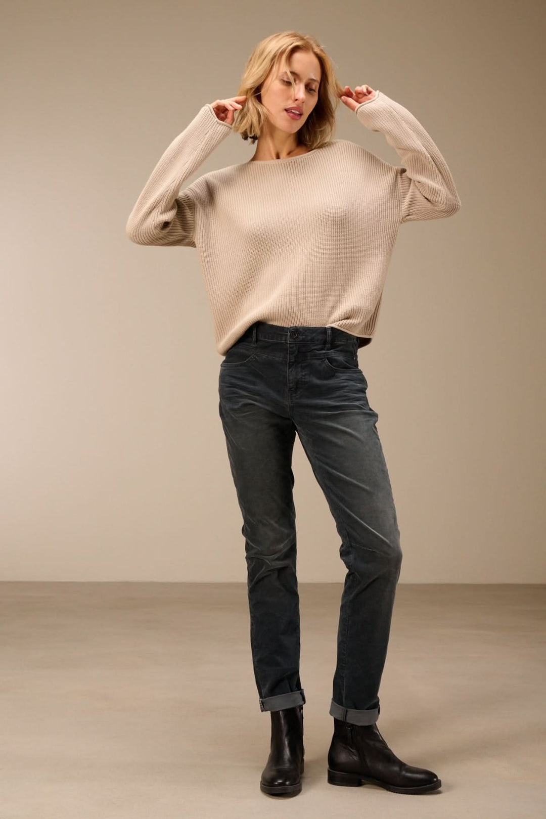 Femme portant un pantalon en velours côtelé coupe ajustée avec un pull beige, style moderne, parfait avec bottines.