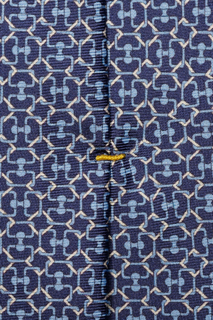 Détail d'une cravate bleue à motif géométrique, avec texture tissée et couture décorative.