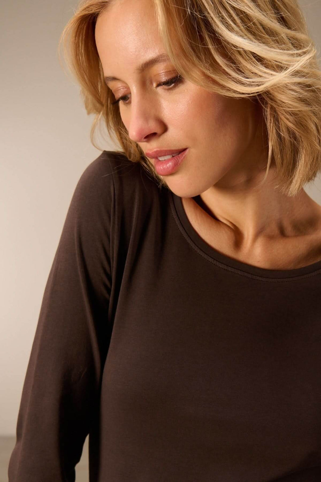 Femme portant un T-shirt manches longues col rond — jersey doux extensible, couleur sombre, coupe confortable et respirante.
