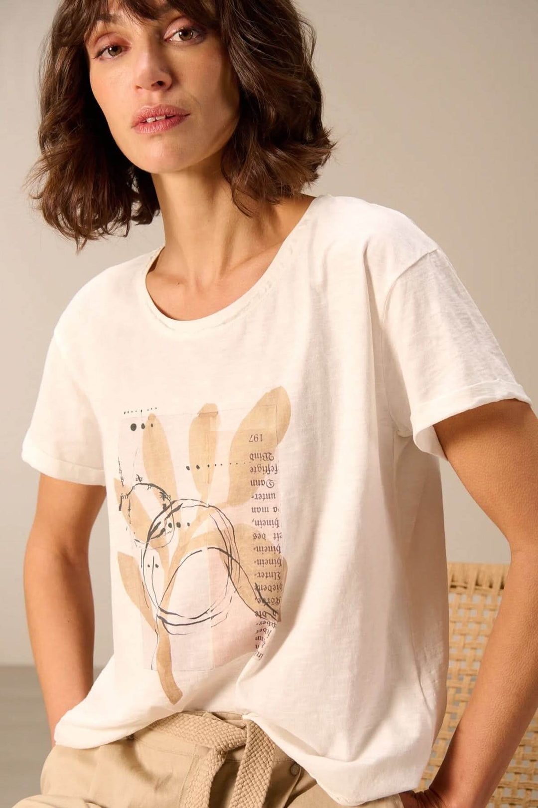 Femme portant un T-shirt à manches courtes coupe décontractée avec design imprimé, assise sur une chaise en rotin.